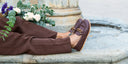 Mocasines chocolate barefoot con cadena de madera con flores sobre una fuente. SHUU Barefoot Calzado barefoot hecho en España.